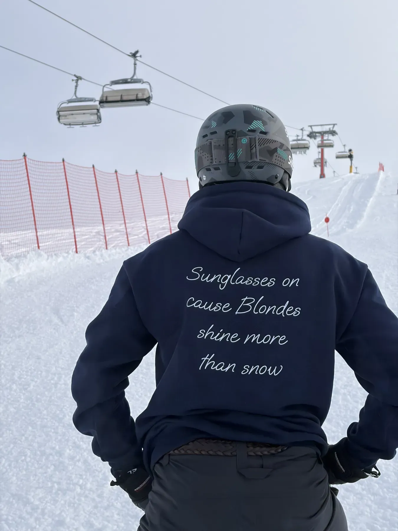 Sciatore di spalle con la felpa blu navy, frase bianca sul retro, sotto la seggiovia